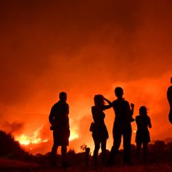Residentes observan las llamas mientras un incendio forestal arrasa cerca de Palaia Fokaia, a unos 45 km al sur de Atenas, Grecia. | Foto:ARIS MESSINIS / AFP