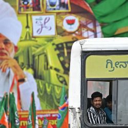 Un pasajero mira por la ventana de un autobús mientras pasa junto a un cartel del primer ministro de la India, Narendra Modi, colocado como bienvenida para inaugurar el nuevo tren de pasajeros Vande Bharat y la Línea Amarilla del Metro Namma en Bengaluru. | Foto:IDREES MOHAMMED / AFP