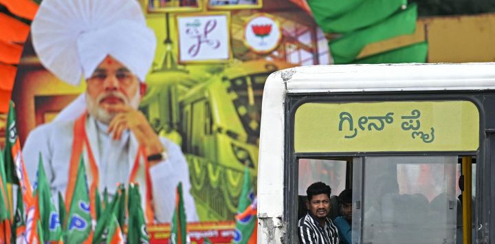 Un pasajero mira por la ventana de un autobús mientras pasa junto a un cartel del primer ministro de la India, Narendra Modi, colocado como bienvenida para inaugurar el nuevo tren de pasajeros Vande Bharat y la Línea Amarilla del Metro Namma en Bengaluru.