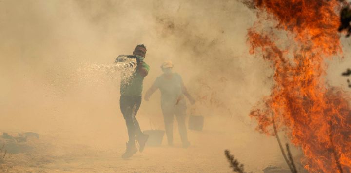 La gente usa cubos de agua para extinguir un incendio forestal que amenaza su casa en el pueblo portugués de Antas, en Trancoso.