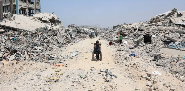 Un niño palestino arrastra una silla de ruedas junto a edificios destruidos en el barrio de Al-Tuffah, en la ciudad de Gaza, tras más de 22 meses de guerra entre Israel y el grupo militante palestino Hamás.