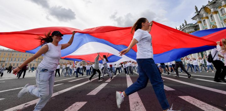 La gente corre con una bandera rusa en la Plaza Dvortsovaya de San Petersburgo, durante el Día de la Bandera Nacional de la Federación Rusa.