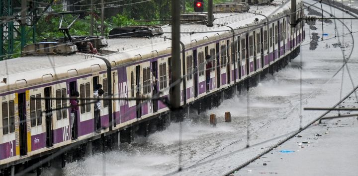 Un tren local circula por una vía férrea inundada durante fuertes lluvias en Mumbai, India.