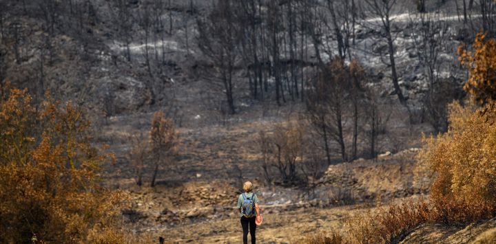 Una mujer camina por un camino a través de tierras arrasadas tras los incendios forestales cerca de la localidad de Fontjoncouse, en el departamento de Aude, en el sur de Francia.