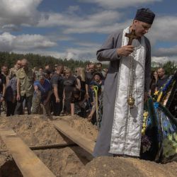 Familiares, amigos y compañeros militares arrojan puñados de tierra sobre el ataúd de la difunta soldado ucraniana del Regimiento de Sistemas No Tripulados "Aquiles", Nataliia Ilnytska, quien murió en un ataque de artillería contra las tropas rusas en la región de Donetsk, mientras un sacerdote reza durante su funeral en Irpin, al noroeste de Kiev, durante la invasión rusa de Ucrania. | Foto:ROMAN PILIPEY / AFP