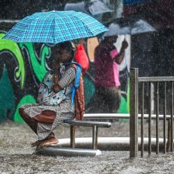 Una colegiala sostiene un paraguas mientras está sentada en un banco durante las fuertes lluvias en Mumbai, India. | Foto:PUNIT PARANJPE / AFP