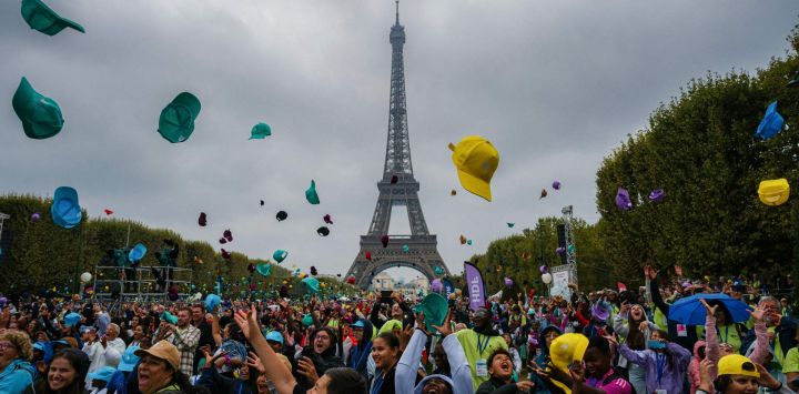 Niños de toda Francia y del extranjero lanzan sus gorras al asistir a un concierto en el Campo de Marte con la Torre Eiffel de fondo en París, como parte de la 46.ª edición de una jornada de actividades para niños que no se van de vacaciones, organizada por la ONG francesa Secours Populaire.