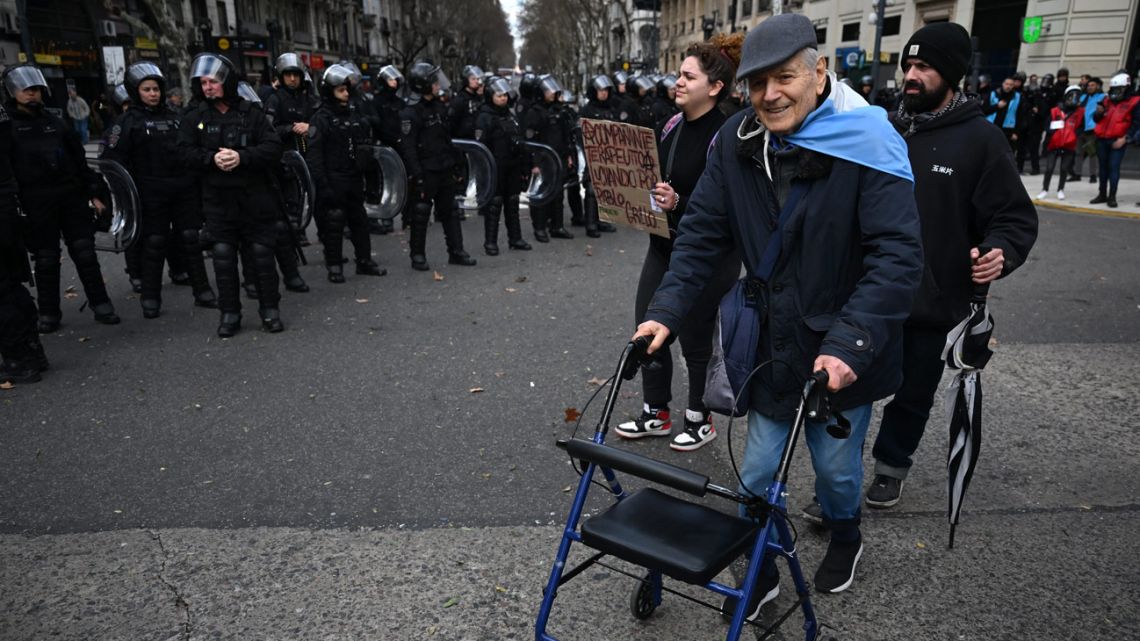 An elderly man walks in front of riot police outside the National Congress in Buenos Aires on August 20, 2025, as deputies debate President Javier Milei’s veto on a bill declaring a disability emergency. 