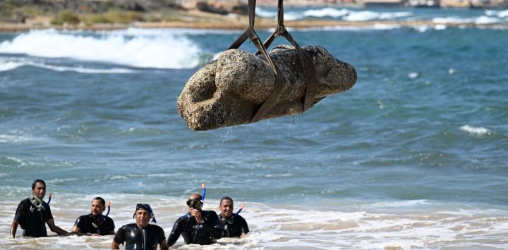 Buzos observan cómo una grúa extrae un artefacto de las aguas de la bahía de Abu Qir, en Alejandría, como parte de un evento organizado por el Ministerio de Turismo y Antigüedades para recuperar antigüedades hundidas.