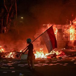 Un manifestante camina con una bandera indonesia frente a una comisaría que fue incendiada y saqueada durante las manifestaciones en Surabaya. | Foto:JUNI KRISWANTO / AFP