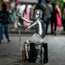 Un niño vestido como Mahatma Gandhi, pintado de color plateado para atraer a los transeúntes, observa mientras pide limosna a los devotos durante el festival Ganesh Chaturthi en Hyderabad, India. | Foto:NOAH SEELAM / AFP
