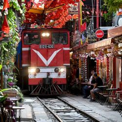 Esta foto muestra un tren pasando por una vía férrea entre terrazas de cafés en el centro de Hanói. Turistas, entusiasmados por el café, se toman selfis a diario en los cafés de Hanói, suavemente iluminados, junto a las vías, emocionados por estar codo con codo con un tren de la época colonial en movimiento, pero no siempre ha sido tan elegante. | Foto:NHAC NGUYEN / AFP