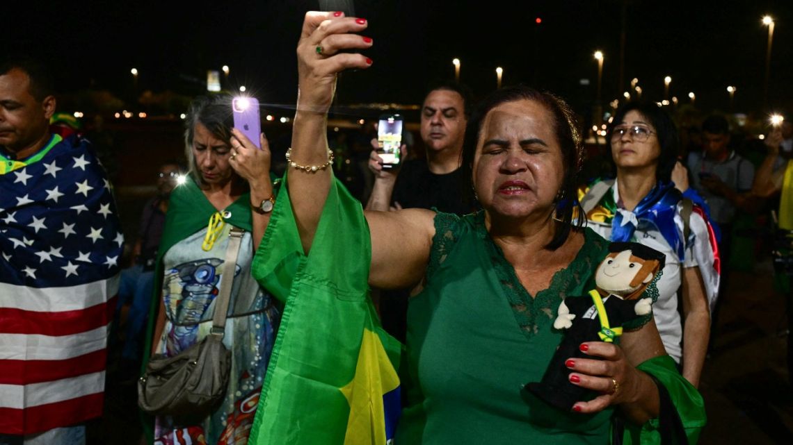 Supporters of former Brazilian President Jair Bolsonaro pray with Brazilian and US flags near his house in Brasilia on September 11, 2025. Brazil's Supreme Court on Thursday sentenced firebrand ex-president Jair Bolsonaro to 27 years in prison for coup plotting at the end of a landmark trial that divided the nation and drew US fury. 