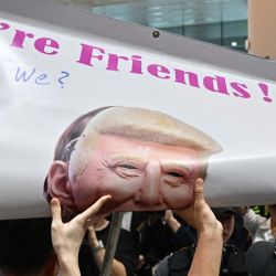 La policía (en primer plano) desenrolla una pancarta con la imagen del presidente estadounidense Donald Trump, exhibida por un manifestante en el Aeropuerto Internacional de Incheon, tras el aterrizaje de un Boeing 747-81 (KE9036) de Korean Air, fletado especialmente para este fin, que transportaba a cientos de trabajadores surcoreanos de regreso desde Atlanta tras su detención en una redada de inmigración estadounidense en una planta de Hyundai-LG en Ellabell, Georgia. | Foto:Anthony Wallace / AFP