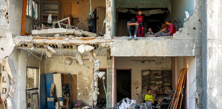 Un hombre y sus hijos se sientan en habitaciones expuestas en un edificio gravemente dañado cerca de la Torre del Soldado Desconocido, destruida por un bombardeo israelí nocturno, en el barrio de Rimal, Ciudad de Gaza.