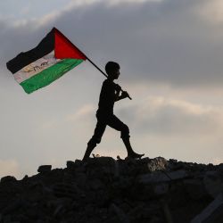 Un niño palestino desplazado ondea una bandera nacional palestina mientras camina sobre los escombros de un edificio destruido en el campamento de refugiados de Bureij, en el centro de la Franja de Gaza. | Foto:Eyad Baba / AFP