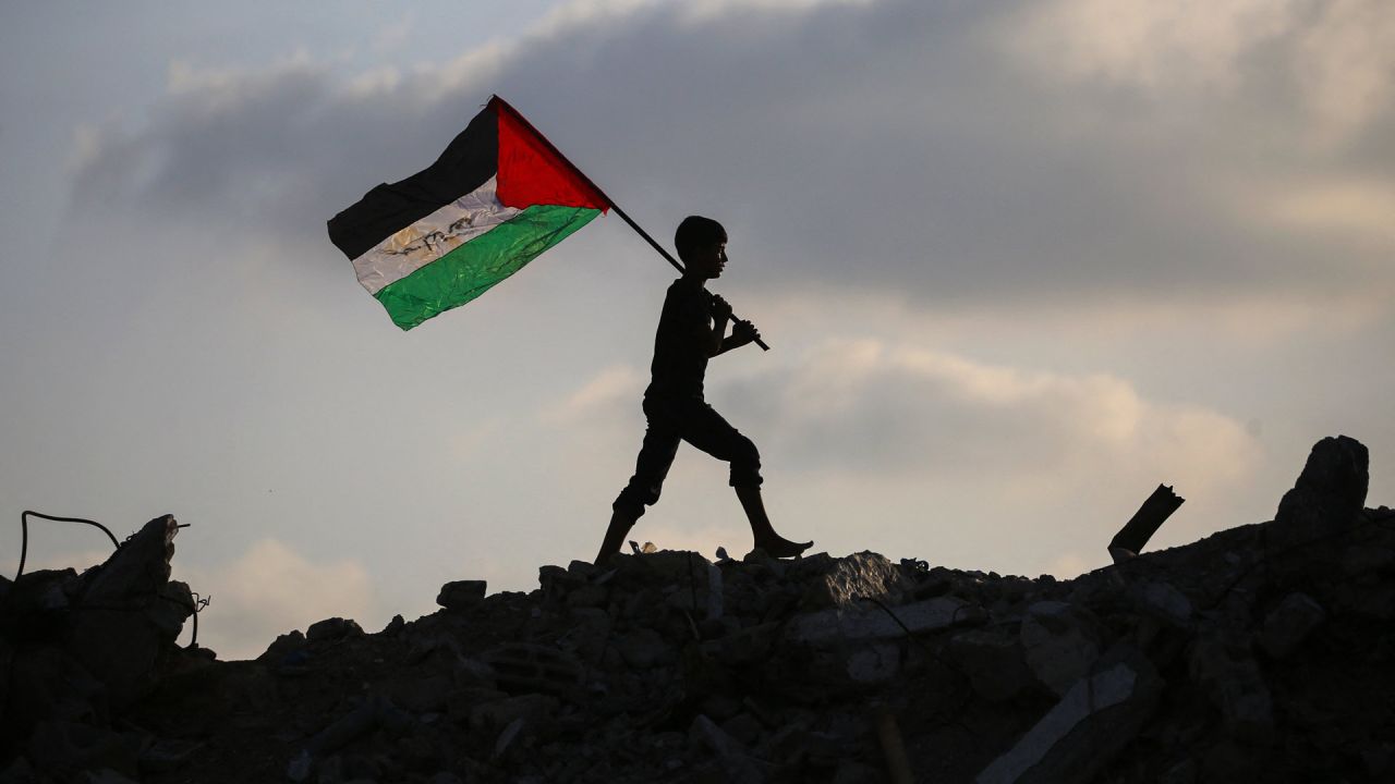 Un niño palestino desplazado ondea una bandera nacional palestina mientras camina sobre los escombros de un edificio destruido en el campamento de refugiados de Bureij, en el centro de la Franja de Gaza. | Foto:Eyad Baba / AFP
