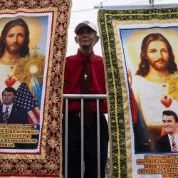 Un partidario de Charlie Kirk y del presidente estadounidense Donald Trump posa con pancartas religiosas frente al estadio State Farm durante el servicio conmemorativo público en honor del activista de derecha Charlie Kirk en Glendale, Arizona. | Foto:ANDREW CABALLERO-REYNOLDS / AFP
