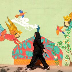 Una mujer pasa junto a un mural en Teherán, la capital iraní. Irán condenó como "injustificable" el restablecimiento de las sanciones de las Naciones Unidas por su programa nuclear, tras el fracaso de las conversaciones con las potencias occidentales y los ataques israelíes y estadounidenses contra sus instalaciones nucleares. | Foto:ATTA KENARE / AFP