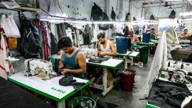Esta fotografía muestra a sastres cosiendo ropa en una pequeña fábrica de ropa dentro de Dharavi, un asentamiento precario en Bombay.