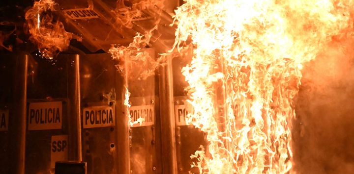 Policías antidisturbios se protegen de bombas molotov durante una protesta por el 11.º aniversario de la desaparición de 43 estudiantes de Ayotzinapa, en la Ciudad de México. En septiembre de 2014, 43 estudiantes de la Escuela Normal Rural de Ayotzinapa desaparecieron tras ser secuestrados en Iguala, Guerrero, México, en lo que se ha calificado como uno de los casos más infames de violación de derechos humanos en México.