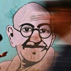 La gente pasa junto a un mural de Mahatma Gandhi con motivo del aniversario del nacimiento de Gandhi, en Varanasi, India. | Foto:NIHARIKA KULKARNI / AFP