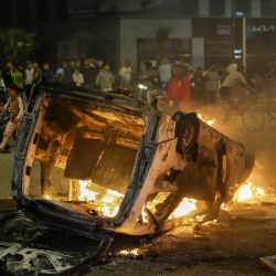 Personas observan un vehículo policial incendiado durante una manifestación liderada por jóvenes que exigían reformas en los sectores de la salud y la educación en Salé. Dos personas murieron cuando agentes abrieron fuego contra un grupo que intentaba asaltar una comisaría en Marruecos, según informaron medios estatales, mientras las protestas, en ocasiones violentas, sacuden al país norteafricano. | Foto:Abdelmajid Bziouat / AFP