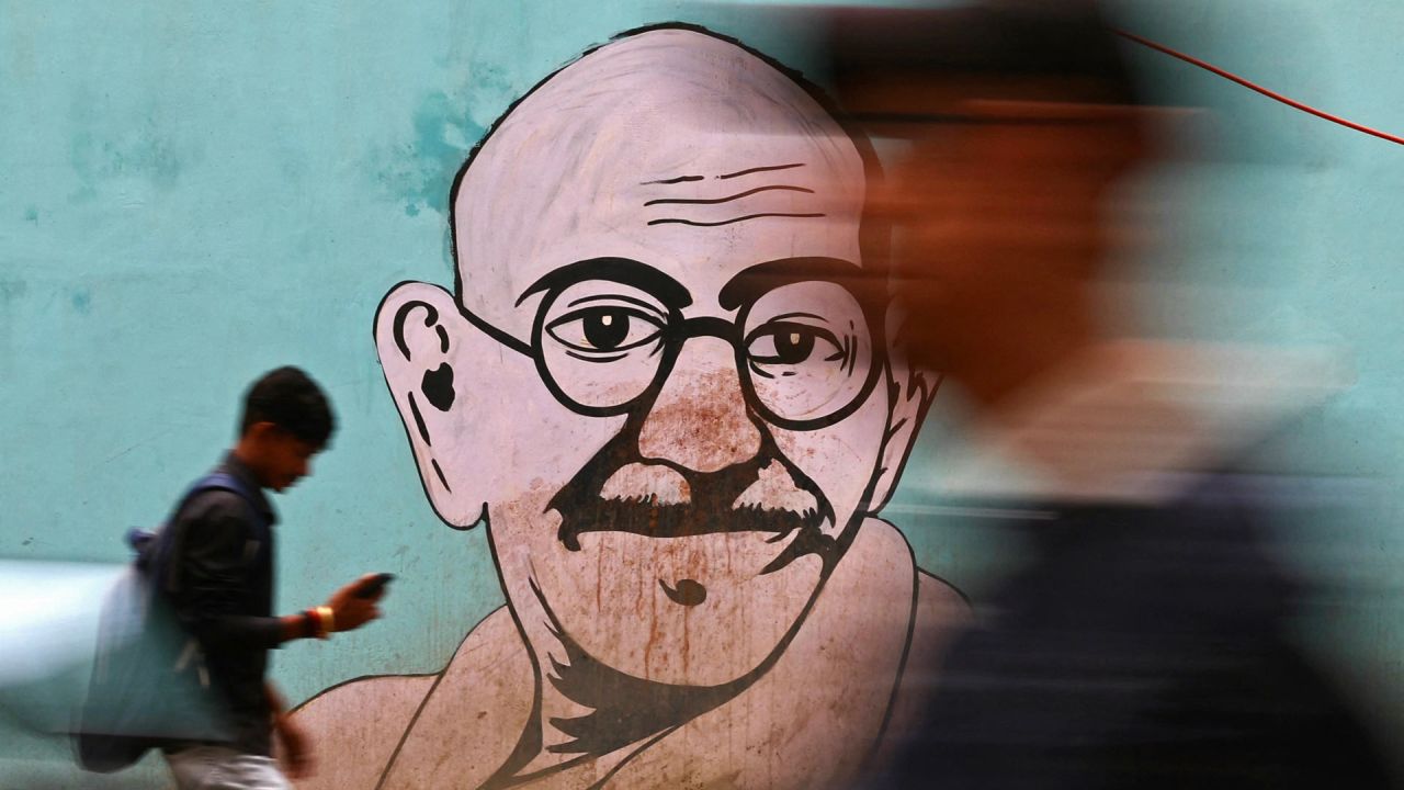 La gente pasa junto a un mural de Mahatma Gandhi con motivo del aniversario del nacimiento de Gandhi, en Varanasi, India. | Foto:NIHARIKA KULKARNI / AFP