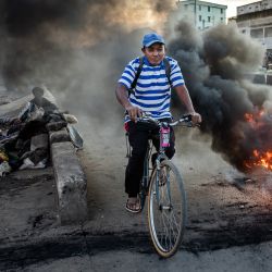 Un hombre pasa en bicicleta junto a un neumático en llamas durante los enfrentamientos entre manifestantes y las fuerzas de seguridad malgaches en una manifestación que exige la dimisión del presidente Andry Rajoelina en Antananarivo. Cientos de personas se manifestaron en Antananarivo, la capital de Madagascar, el martes, duodécimo día de un movimiento de protesta liderado por jóvenes que ha sumido al país en una crisis política. | Foto:LUIS TATO / AFP
