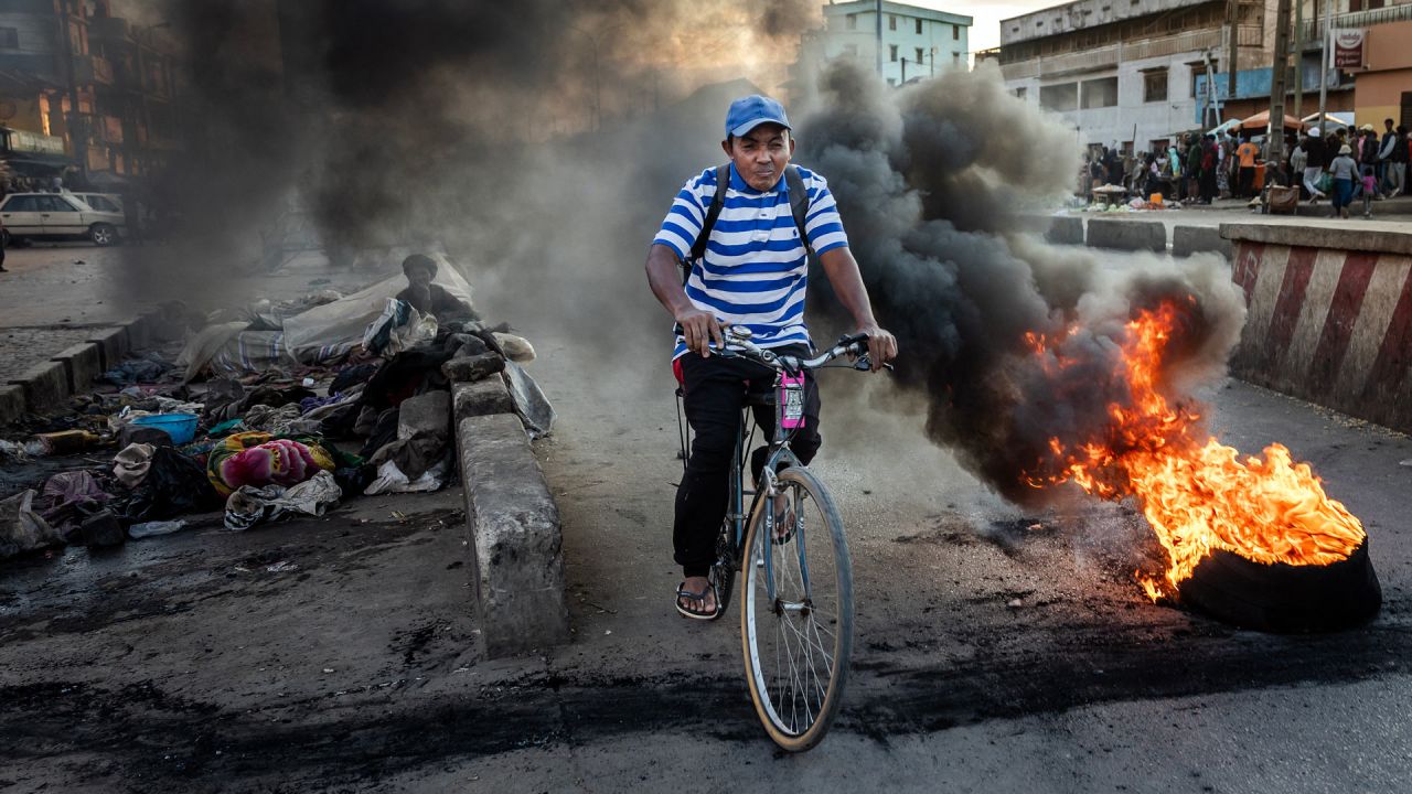 Un hombre pasa en bicicleta junto a un neumático en llamas durante los enfrentamientos entre manifestantes y las fuerzas de seguridad malgaches en una manifestación que exige la dimisión del presidente Andry Rajoelina en Antananarivo. Cientos de personas se manifestaron en Antananarivo, la capital de Madagascar, el martes, duodécimo día de un movimiento de protesta liderado por jóvenes que ha sumido al país en una crisis política. | Foto:LUIS TATO / AFP