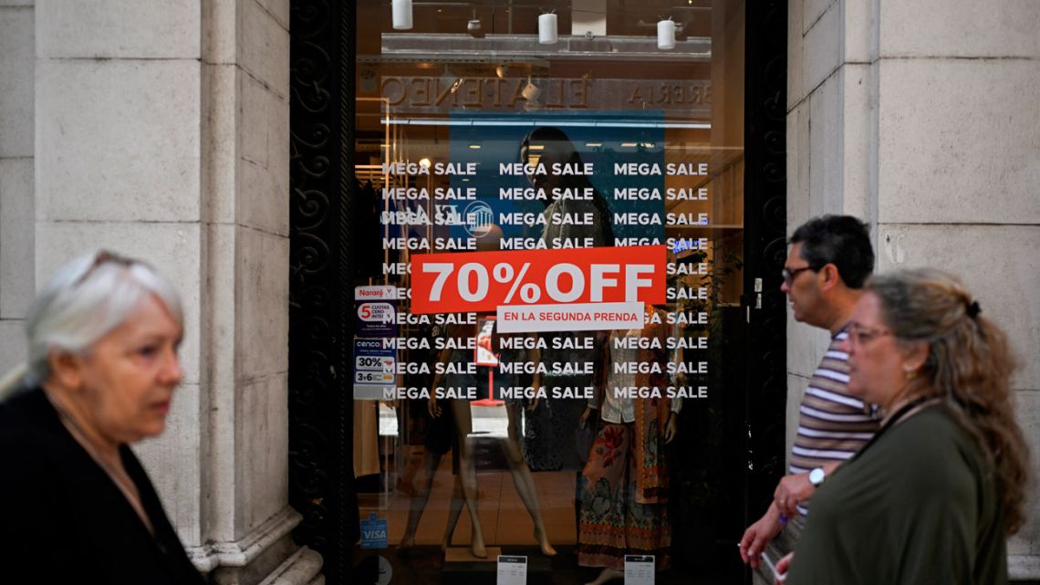 People walk past a store window featuring a discount sign in Buenos Aires on October 14, 2025. 