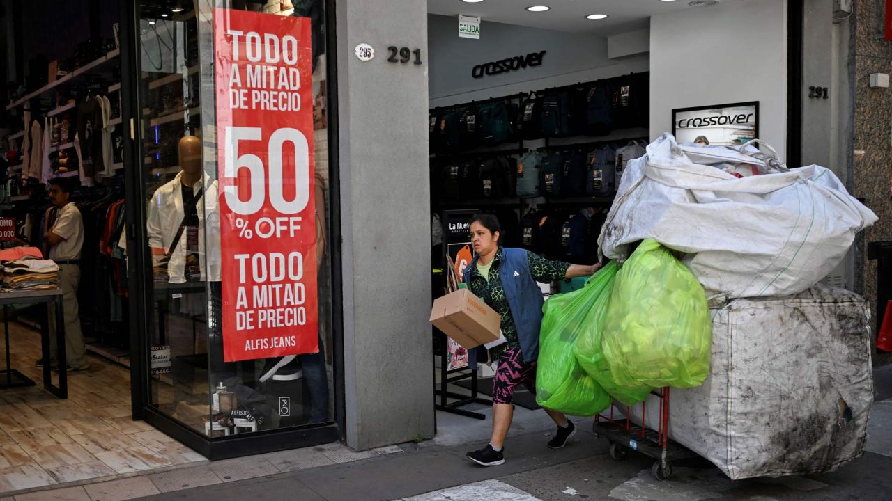 Una recicladora arrastra su carrito frente a un local con un cartel de descuento en Buenos Aires. | Foto:LUIS ROBAYO / AFP