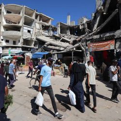 Palestinos caminan junto a un edificio destruido en un mercado improvisado en el campo de refugiados de Nuseirat, ubicado en el centro de la Franja de Gaza, tres días después de la entrada en vigor del alto el fuego. | Foto:Eyad Baba / AFP