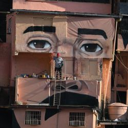 Un hombre trabaja frente a un mural gigante del doctor venezolano José Gregorio Hernández, también conocido como "el médico de los pobres", pintado en las casas de la comunidad El Samán de Bolívar, en el barrio de Petare, Caracas, Venezuela. | Foto:Federico Parra / AFP