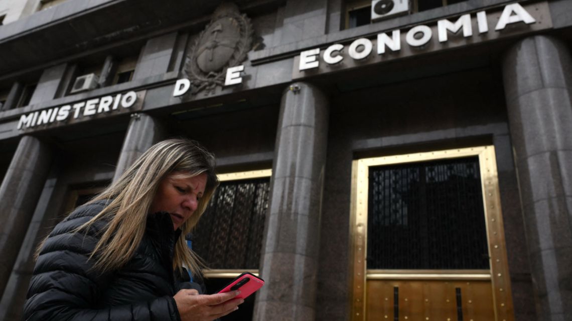 A woman checks her mobile phone as she walks past the Economy Ministry in Buenos Aires, on October 27, 2025. 