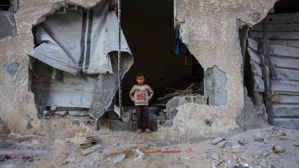 Un niño permanece de pie en una abertura de la pared de su casa, destruida en un ataque israelí en Jan Yunis