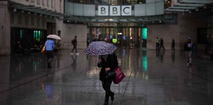 Personas se resguardan de la lluvia frente a la entrada de la BBC en Londres. Foto de HENRY NICHOLLS / AFP