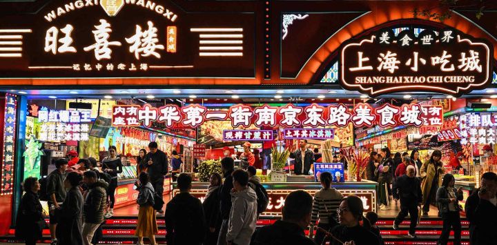 Personas caminan frente a tiendas de comida en una calle peatonal del distrito de Huangpu en Shanghái. Foto de Hector RETAMAL / AFP