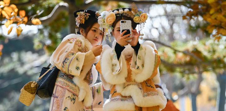 Dos mujeres vestidas con trajes tradicionales se toman una selfie mientras caminan por un sendero en Beijing. Foto de WANG Zhao / AFP