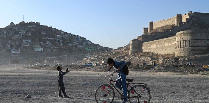 Niños afganos montan una bicicleta y vuelan una cometa cerca del lago Shuhada en Kabul. Foto de Wakil KOHSAR / AFP