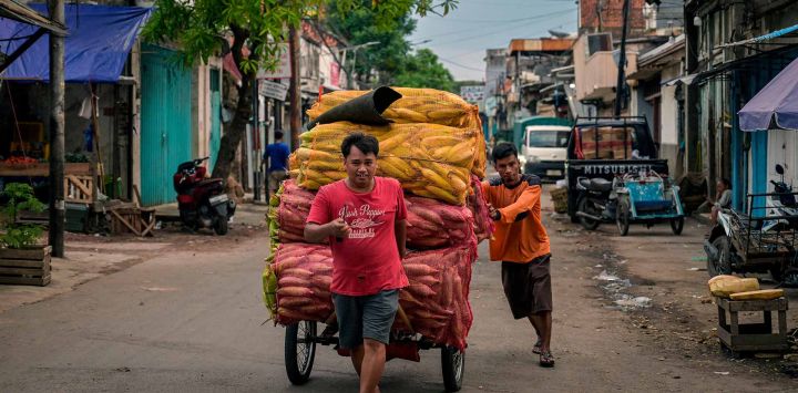 Trabajadores empujan un becak cargado con sacos de maíz en un mercado tradicional de verduras en Surabaya. Foto de JUNI KRISWANTO / AFP