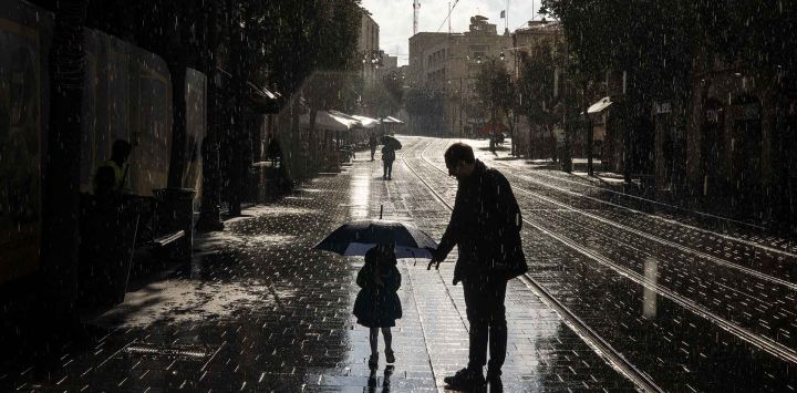 Una joven camina por una calle con un paraguas mientras caen las primeras lluvias de invierno en Jerusalén. Foto de John Wessels / AFP