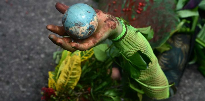 Un hombre indígena se acuesta en el suelo mientras sostiene un globo en la mano durante la "Marcha Global de Pueblos Indígenas". COP30. Brasil. Foto de Pablo PORCIUNCULA / AFP
