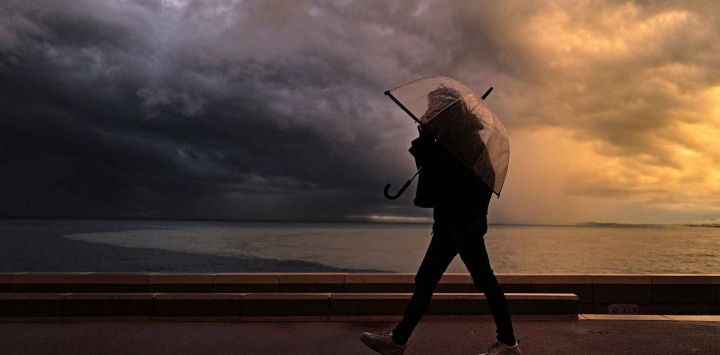 Un peatón camina con un paraguas junto al mar Mediterráneo durante las fuertes lluvias en la ciudad de Niza, en la Riviera francesa. Foto de Valery HACHE / AFP