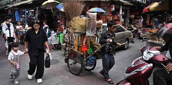 Un vendedor guía un carrito lleno de escobas y artículos de limpieza del hogar por el área de Chinatown en Bangkok. Foto de Lillian SUWANRUMPHA / AFP