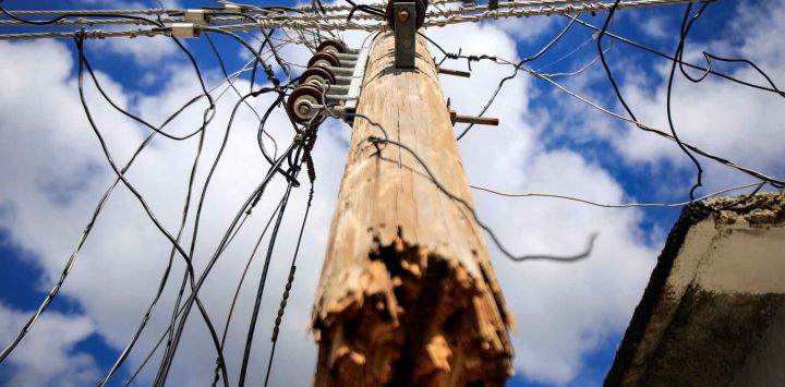 Un poste de electricidad roto por el huracán Melissa cuelga suspendido de los cables en El Cobre, Santiago de Cuba. Foto de AFP