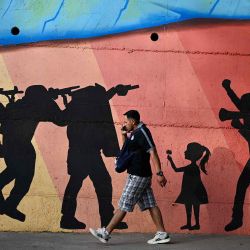 Un hombre pasa frente a un mural que muestra a hombres armados apuntando a manifestantes, aludiendo a la represión policial, en una avenida de Tegucigalpa. Foto de Orlando SIERRA / AFP | Foto:AFP