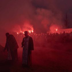Sacerdotes ucranianos permanecen de pie mientras los dolientes encienden bengalas durante el funeral de Artur Vilchynskyi. Foto de Roman PILIPEY / AFP | Foto:AFP