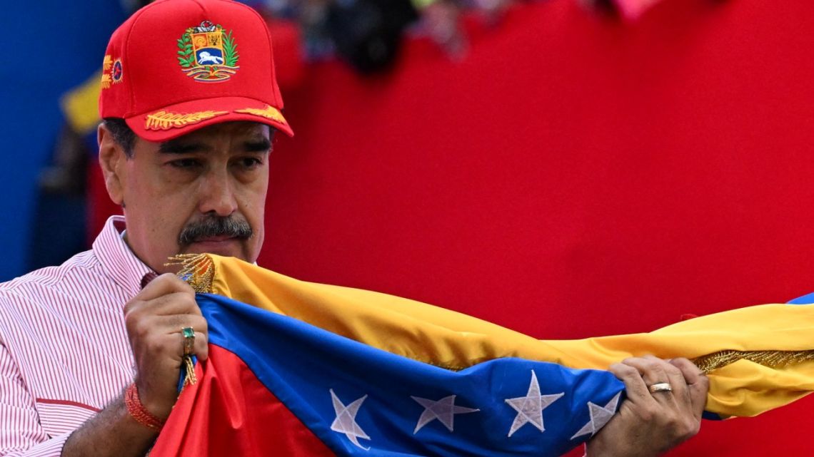 Venezuela’s President Nicolas Maduro holds the national flag during a rally in Caracas on December 1, 2025.