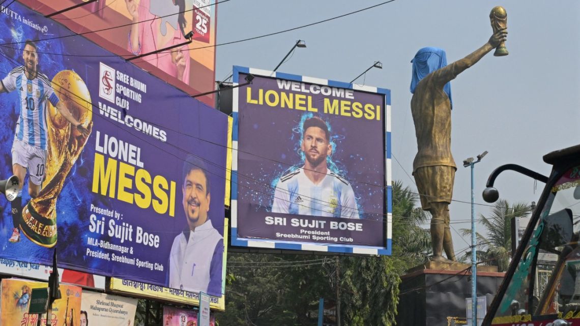 Commuters cross promotional posters and veiled statue of Inter Miami's Argentine forward number 10 Lionel Messi, on the eve of his visit, in Kolkata on December 12, 2025. Lionel Messi will unveil a 70-foot statue of himself in India on December 13 as he embarks on a three-day trip of the country that has sparked a fan frenzy. 